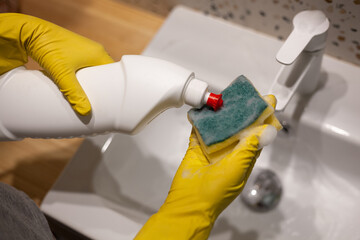 Female hands cleaning bathroom washing washbasin in protective gloves at home