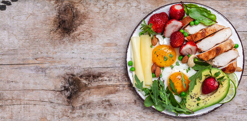 Plate with keto diet food. Keto breakfast Fried egg, avocado, strawberry, grilled chicken fillet, cheese, nuts and arugula, Ketogenic diet. Healthy food concept, top view