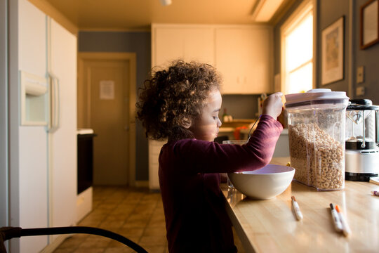 Girl eats cereal in sunlit kitchen
