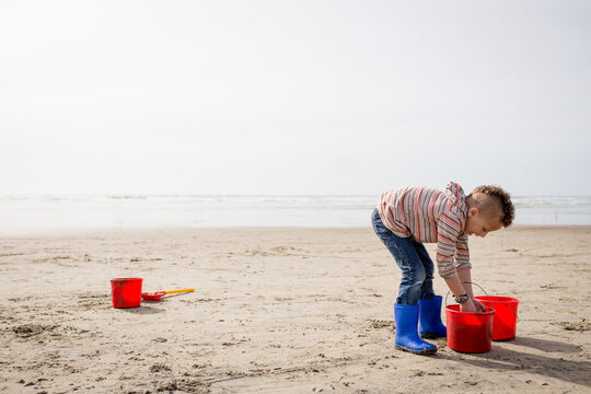 Boy fills buckets with sand on beach