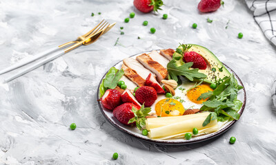 Plate with keto diet food. Keto breakfast Fried egg, avocado, strawberry, grilled chicken fillet, cheese, nuts and arugula, Ketogenic diet. Healthy food concept, top view