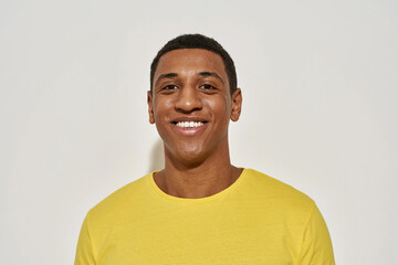 Portrait of joyful young mixed race man in casual yellow t shirt smiling at camera while posing isolated over gray background