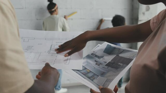 Close up shot of unrecognizable African-American parents looking at blueprint and home remodeling plans while their children measuring wall