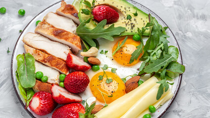Fried egg, avocado, strawberry, grilled chicken fillet, cheese, nuts and arugula. Keto diet. Healthy breakfast or lunch. top view.