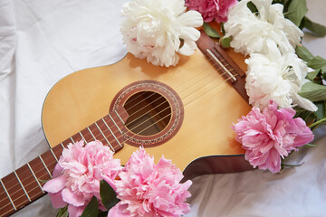 An acoustic wooden guitar lies on a white sheet surrounded by pink and white peonies. - obrazy, fototapety, plakaty