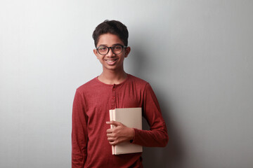 Portrait of a happy young boy holding books against a grey wall