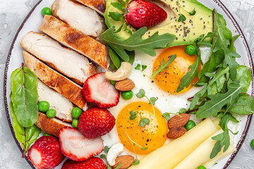 Fried egg, avocado, strawberry, grilled chicken fillet, cheese, nuts and arugula. Ketogenic diet. Healthy food concept, top view