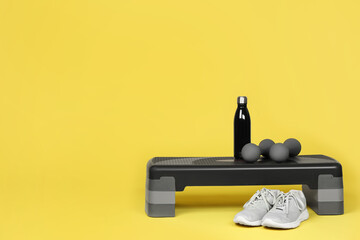 Step platform, dumbbells, water bottle and sneakers on yellow background, space for text. Sport...
