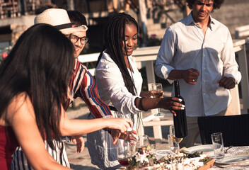 Diverse group of friends carry food and wine to the outdoor dinner table.