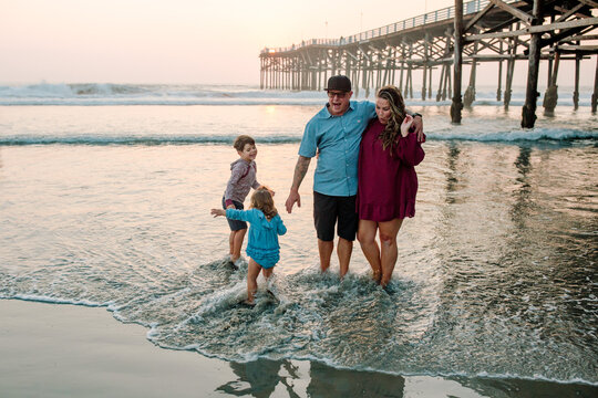 Family playing in surf near pier at sunset