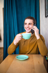Talking with friends. Confident young man talking on the mobile phone and smiling while sitting in cafe