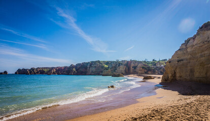 Praia da Dona Ana Beach, sandy beach with clear blue water between cliffs on a sunny day, no...