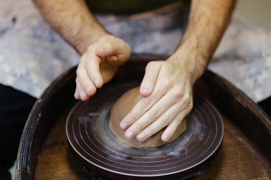 Hands with clay and potter's wheel in workshop 