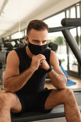 Young athletic man wearing a prevention face mask during his workout in the gym