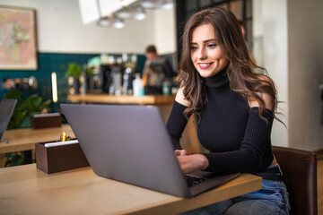 Beautiful young woman working on laptop and smiling while sitting in cafe