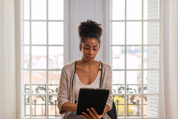 Black woman browsing tablet in cozy room