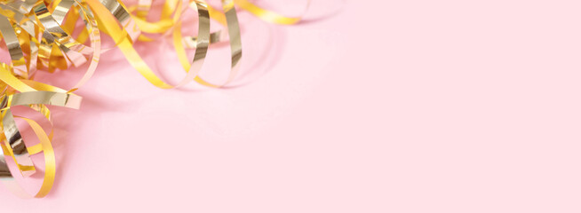 Shiny golden serpentine streamers on pink background. Banner with copy space. Top view, flat lay