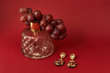 Studio shot of epoxy resin earrings with golden foil inside, carafe and a bunch of grapes isolated over red background