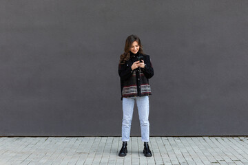 Portrait of smiling pretty girl using mobile phone, smiling at smartphone display, use app to order taxi, messaging on her way to party, stand on street in glasses and denim jacket