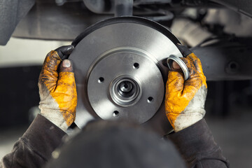 Closeup male tehnician mechanic greasy hands in gloves install new car oem brake steel rotor disk...