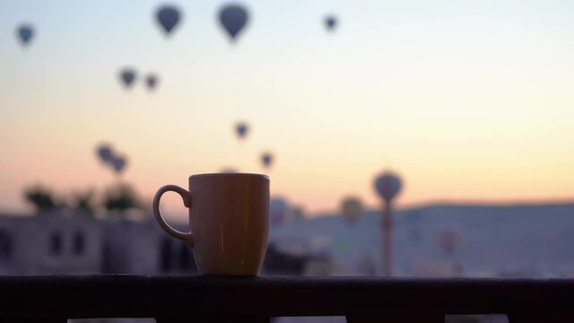 Making tea. Closeup view 4k of cup standing on wooden surface isolated on real blurry flying hot air balloons in Goreme city, Cappadocia, Turkey. Gorgeous morning scenic sunrise and tourism concept