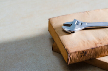 A blurry picture of a hand tool called a slotted wrench, which is made of metal with a glossy finish Placed on the back of an old book that is being lit by the light. (Blur)