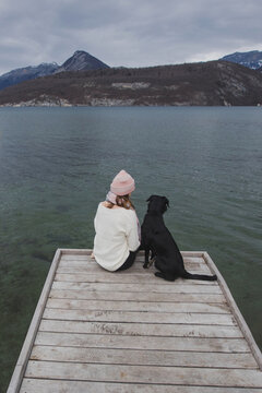friendship, woman and her dog sitting on wooden pier in winter day