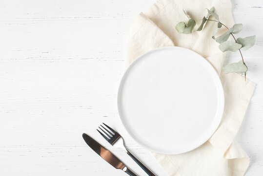 An empty plate and cutlery on a white wooden table. Top view.