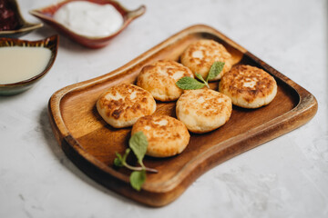 Syrniki served with sweet milk and jam on a white table.