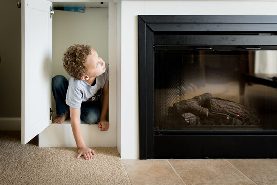 Boy peeks out of cupboard by fireplace