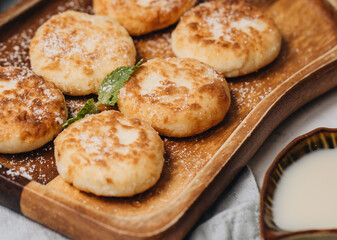 Syrniki served with sweet milk and jam on a white table.