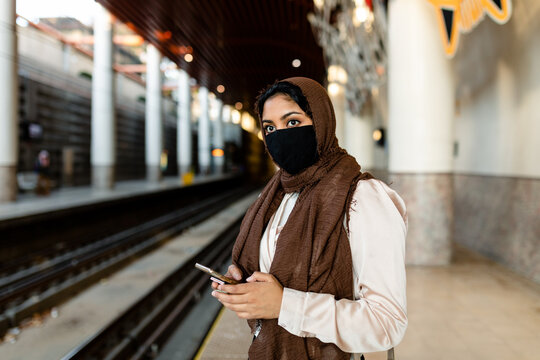Masked Muslim Woman Checks Phone at Train Station