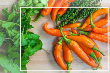 Images of various Thai traditional vegetables placed on a wooden board such as yellow chili pepper, bitter bean,  green peppercorns, holy basil leaves.