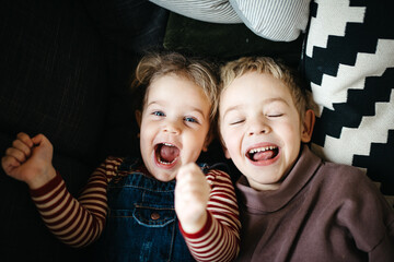 Brother and sister laying down in a sofa and laughing and screaming at camera