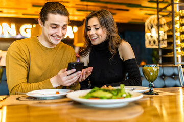 Couple in restaurant eating lunch and looking on smartphone