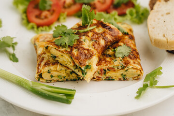 Omelette with tomatoes, bread and coriander on white plate.