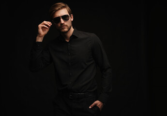Obraz premium Men in full suit. Confident young businessman in sunglasses standing isolated on black.