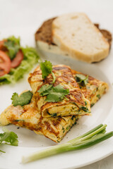 Omelette with tomatoes, bread and coriander on white plate.