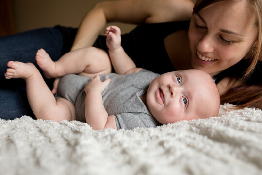 Smiling baby wriggles on bed with mom
