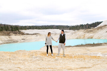 American couple holding hands on a panoramic background of blue lake, sand and forest