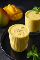 Mango lassi or fruits smoothies on a black background, close up. Heathy ayurvedic cold mango lassi made of yogurt, water, spices, fruits and ice.
