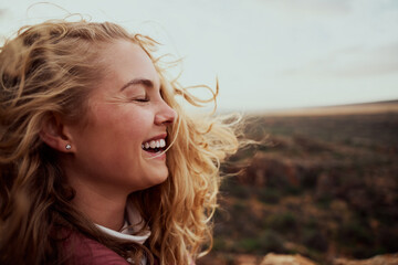Side view of beautiful young woman feeling windy breeze touching face with hair flying