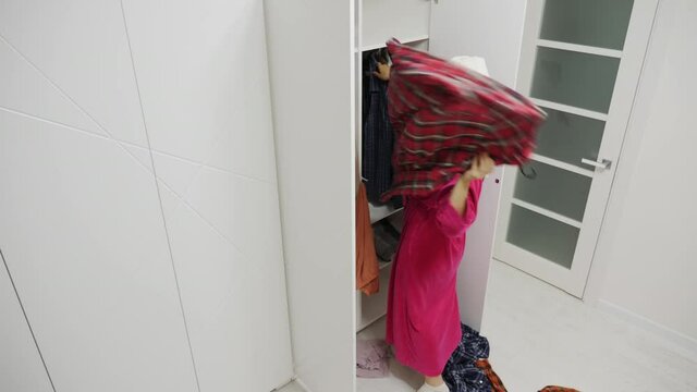 Annoyed woman in a bathrobe after a quarrel with her husband throws men's clothes out of a white wardrobe