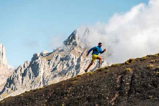 Adult sportsman running uphill in mountains on foggy day 