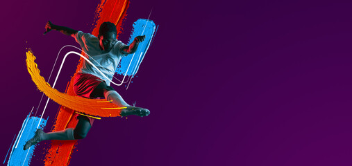 African soccer football player jumping isolated on purple neon background. Flyer. Vibrant colors