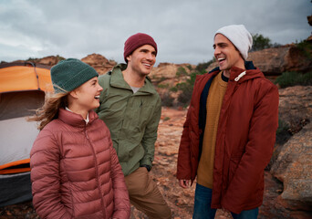 Cheerful young male and female friends in winter clothing laughing during camping on mountain hill