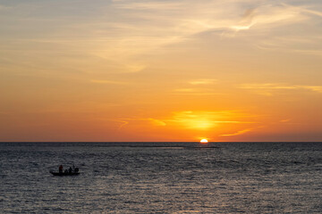 Naklejka premium Sun sets on the ocean with a fishing boat in silhouette.