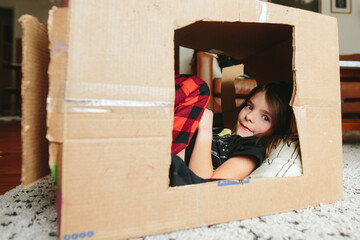 little girl lays down inside cardboard box fort
