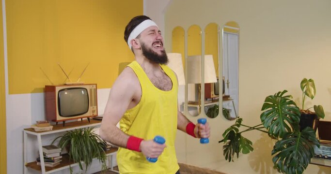 Training hard. Waist up portrait view of the tired bearded man running with dumbbells while training hard at his own flat. Sport and workout concept