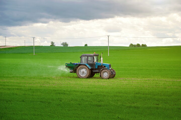 Tractor spray fertilizers on green field, agriculture wallpaper. Farmer spreading potash...